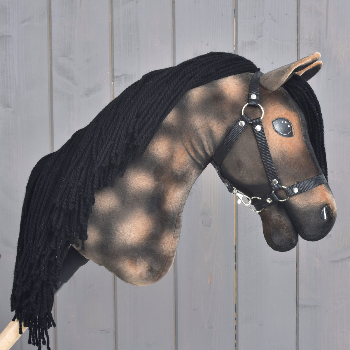 Hobby Horse Stormy s černou ohlávkou od Hobby Horse LarDen, ručně vyrobený Hobby Horse inspirovaný hannoverským hřebcem s hnědo-černě malovanou tváří, černou přízovou hřívou a černou ohlávkou, na pozadí šedého dřeva.