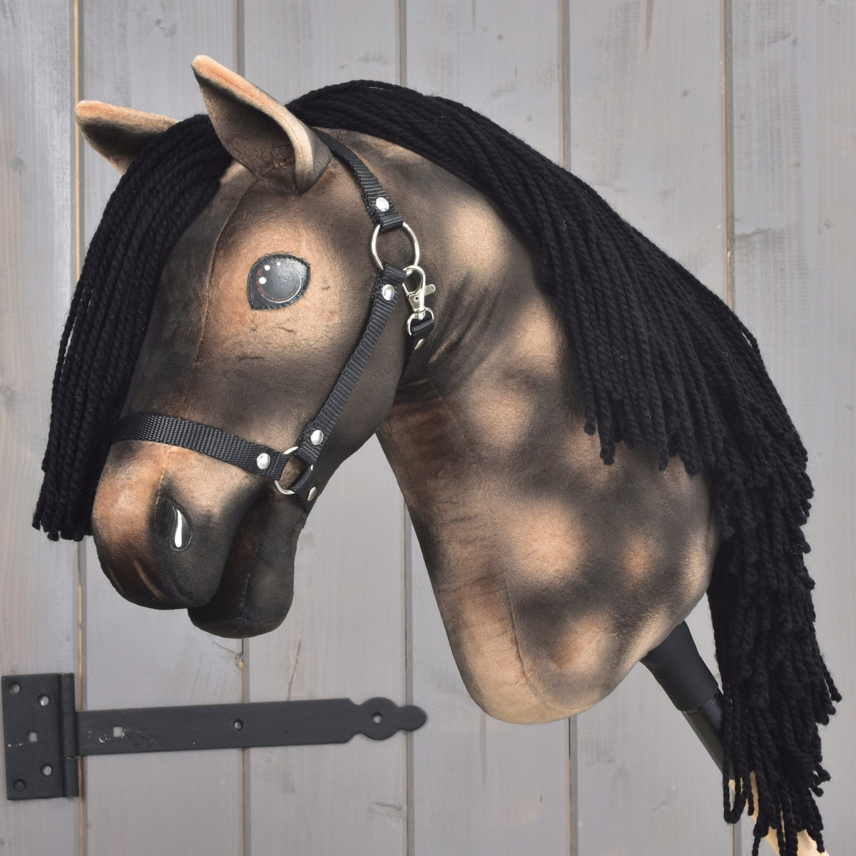 Hobby Horse Stormy s černou ohlávkou od Hobby Horse LarDen s hnědou plyšovou hlavou, černou přízovou hřívou, černou ohlávkou a lesklýma knoflíkovýma očima, nasazený na dřevěné tyči na světlém dřevěném pozadí, okouzlující kousek inspirovaný duchem hannoverského hřebce.