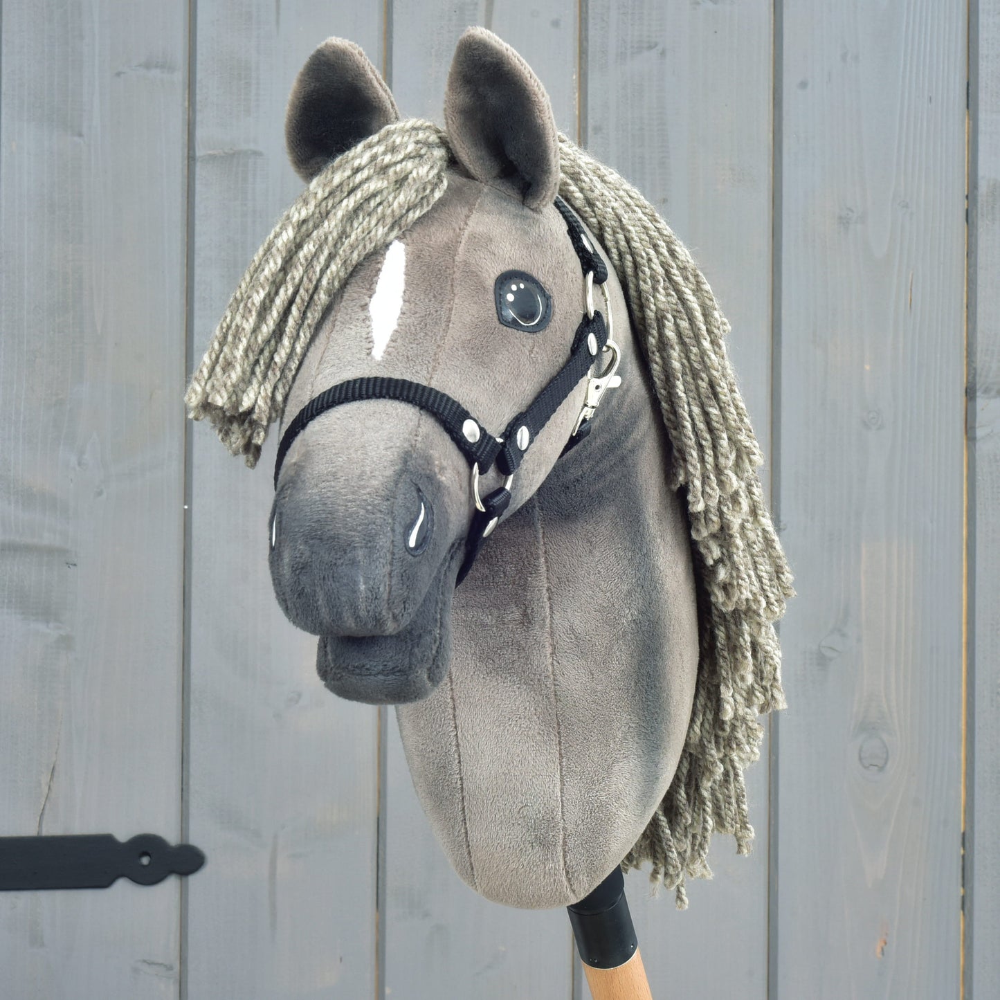 Hobby Horse Swing s černou ohlávkou - velikost S od Hobby Horse LarDen, detail elegantního šedého provedení s přízí hřívou, knoflíkovýma očima, výraznou bílou lysinou na obličeji a černou ohlávkou, připomínající vytříbený vzhled hanoverského hřebce, na dřevěném pozadí.