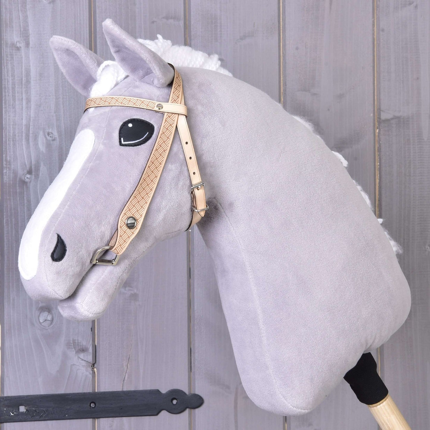 Hobby Horse LarDen Uzdečka western Classic, světle šedý plyšový Hobby Horse s bílou lysinou a černýma očima na dřevěné tyči, se stylovou westernovou uzdečkou na pozadí z šedých dřevěných prken.