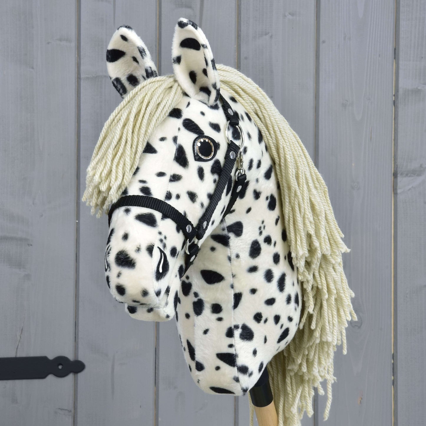 Hobby Horse Lord Valentine s černou ohlávkou od Hobby Horse LarDen, s černobílou strakatou srstí, přízovou hřívou a černou ohlávkou, na pozadí šedého dřeva.