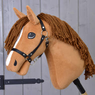 Hobby Horse Wendy s černou ohlávkou od Hobby Horse LarDen je plyšová hračka inspirovaná ryzkou klisnou s hnědou hřívou z příze, bílým pruhem na obličeji a černou ohlávkou – ideální pro nápaditou hru – zobrazená před dřevěným panelovým pozadím.