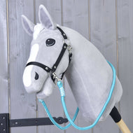 Hobby Horse LarDen Otěže Atlantis na šedém plyšovém Hobby Horse s černou uzdečkou a modrými polypropylenovými lanovými otěžemi, na dřevěné tyči před rustikální dřevěnou stěnou.