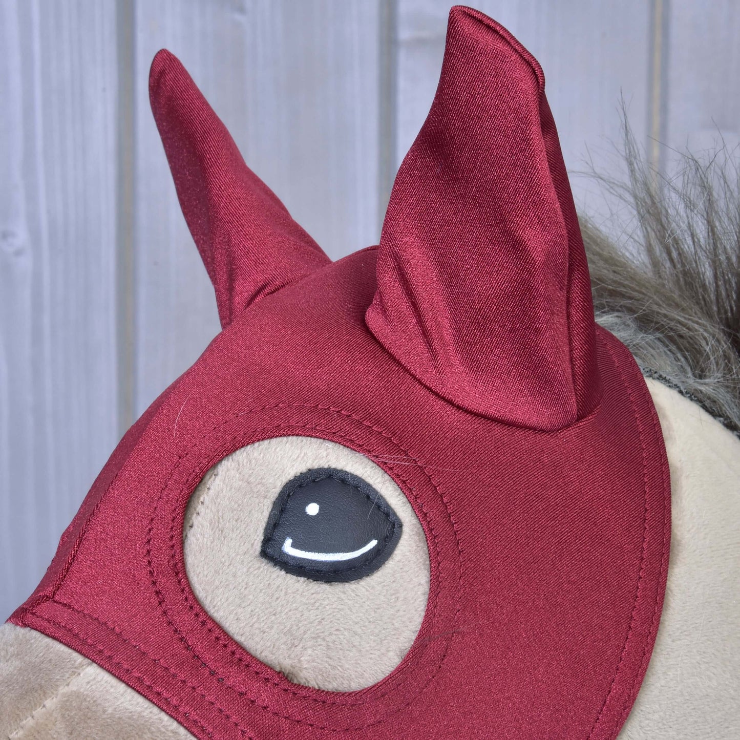 Detail plyšové hračky Hobby Horse LarDen s Maska Barn Red, se špičatými ušima a šedou hřívou, na světlém dřevěném pozadí.