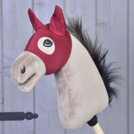 Maska Barn Red od Hobby Horse LarDen s světle hnědým obličejem, černou hřívou a červenou stájovou uzdečkou, nasazená na tyči před šedými dřevěnými prkny.