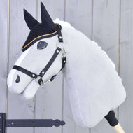 Šedý Hobby Horse LarDen s černými otěžemi a bílou hřívou má na sobě čabraku háčkovanou Black Gold pro ochranu proti hmyzu, s černými detaily obličeje, na světle dřevěném pozadí.