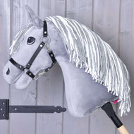 Šedý Hobby Horse Calypso s černou ohlávkou od Hobby Horse LarDen, inspirovaný holandským teplokrevníkem, má bílou přízovou hřívu a je nasazený na dřevěné tyči, opřený o světle zbarvenou dřevěnou stěnu.