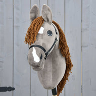 Hobby Horse Chanell s černou ohlávkou od Hobby Horse LarDen, se šedou srstí, hnědou přízovou hřívou, bílými skvrnami na obličeji a velkýma výraznýma očima, zobrazený na pozadí šedého dřeva.