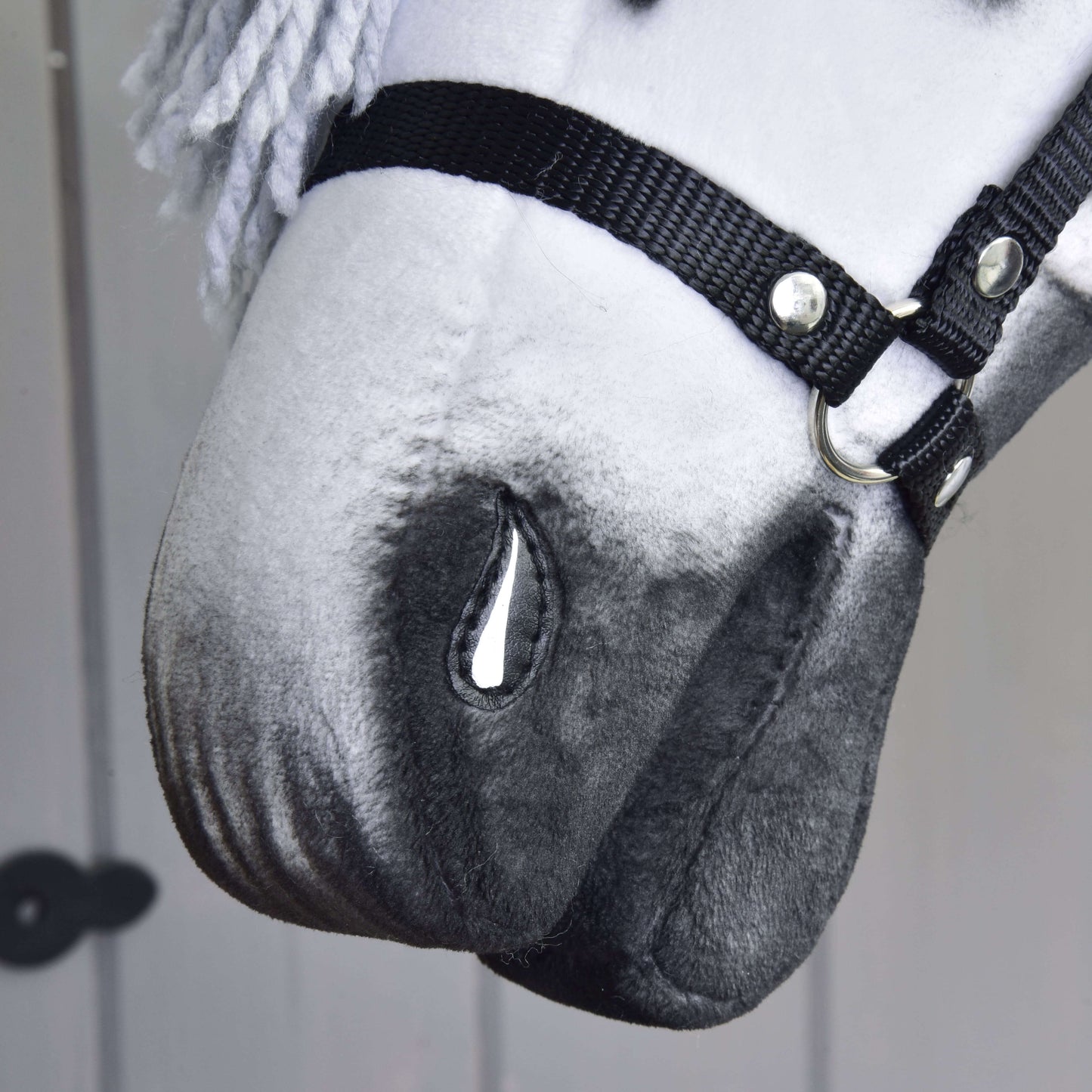 Detail ručně vyrobeného Hobby Horse Chantal s černou ohlávkou od Hobby Horse LarDen, s bílo-šedým zbarvením, malovaným detailem slzy, přízovou hřívou a neutrálním pozadím.