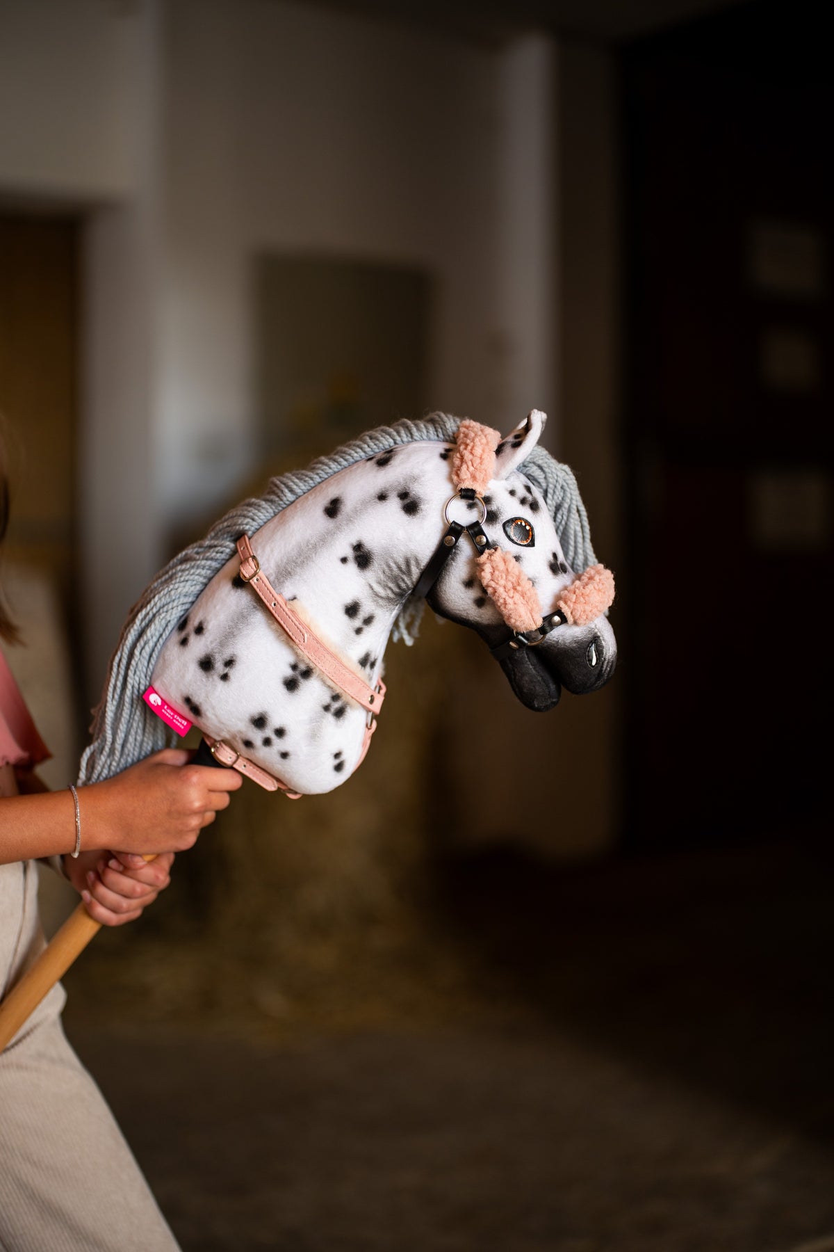 Hlava a krk Hobby Horse Chantal s černou ohlávkou od Hobby Horse LarDen držené ve stáji, bílý plyš s černými leopardími skvrnami, šedá přízová hříva, černý čenich, s ohlávkou Old Rose s kožešinou z koženky a náprsníkem s kožešinou