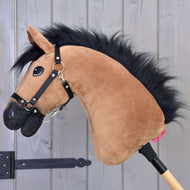 Hobby Horse Cookie s černou ohlávkou od Hobby Horse LarDen s plyšovým světle hnědým obličejem, černou hřívou a černou ohlávkou na dřevěné tyči, ideální pro fanoušky parkuru, zobrazený na pozadí šedého dřeva.