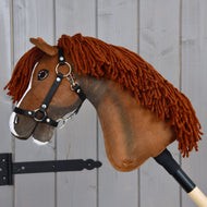 Hobby Horse Cooper s černou ohlávkou od Hobby Horse LarDen s hnědou látkovou hlavou, přízovou hřívou a bílou lysinou na nose, upevněný na dřevěné tyči. Je stylizovaný jako elegantní sportovní kůň, ideální pro kreativní drezurní dobrodružství, a zde vyfotografovaný na šedém dřevěném pozadí.