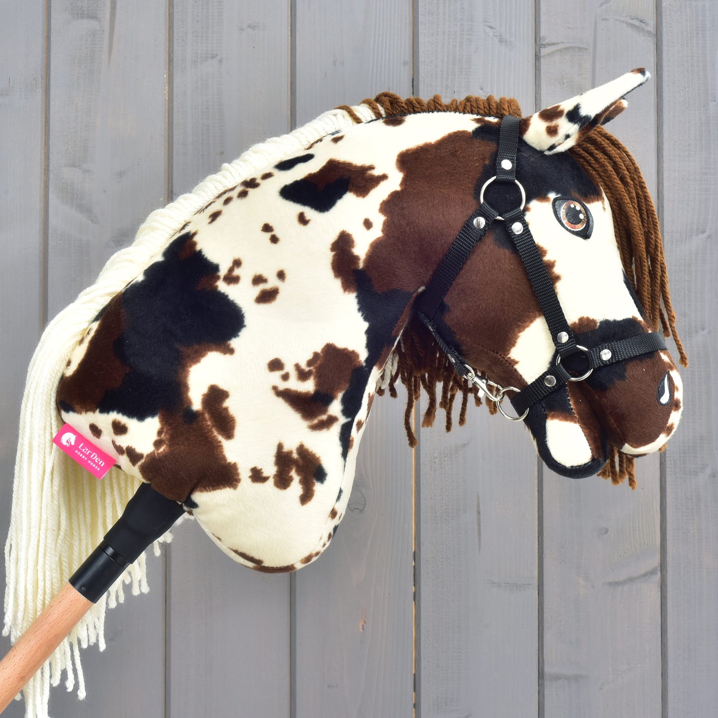 Hobby Horse Dakota s černou ohlávkou od Hobby Horse LarDen zachycuje nezkrotného ducha mustanga svým hnědobíle skvrnitým plyšovým provedením, černou ohlávkou a přízovou hřívou. Je upevněný na dřevěné tyči a zobrazený na pozadí světlých dřevěných prken připomínajících otevřené pláně Severní Ameriky.
