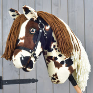 Hobby Horse Dakota s černou ohlávkou od Hobby Horse LarDen, plyšový model inspirovaný mustangem, s hnědou přízovou hřívou, černou ohlávkou a hnědobílou skvrnitou srstí zachycující divokého ducha Severní Ameriky, na dřevěném pozadí.