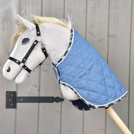 Plyšový Hobby Horse na dřevěné tyči má na sobě deku Beautiful Jeans od Hobby Horse LarDen a černou ohlávku, umístěný před světlou dřevěnou stěnou pro dodatečnou ochranu.