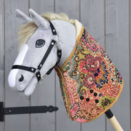 Hobby Horse LarDen „Deka Jungle“ je plyšový Hobby Horse se šedou hlavou, černou uzdečkou a barevným dekovým tělem — ideální pro imaginativní hru nebo raný trénink s koněm — zobrazený před pozadím z dřevěných panelů.