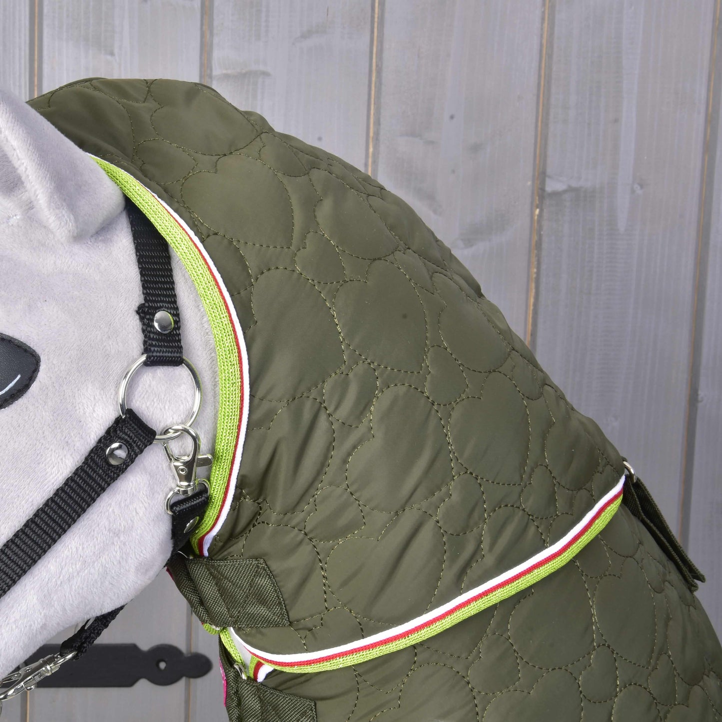 Detail psa v Deka s odepínatelným krkem Rubby od Hobby Horse LarDen v olivově zelené barvě s neonově zeleným zipem a bílo-červeným lemováním, stojícího před šedým dřevěným pozadím.