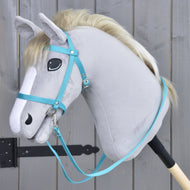 Uzdečka z popruhu Turquoise od Hobby Horse LarDen na šedém plyšovém hobby horse se světlou hřívou, s černou uzdečkou a otěžemi, nasazeném na dřevěné tyči před šedým dřevěným plotem.