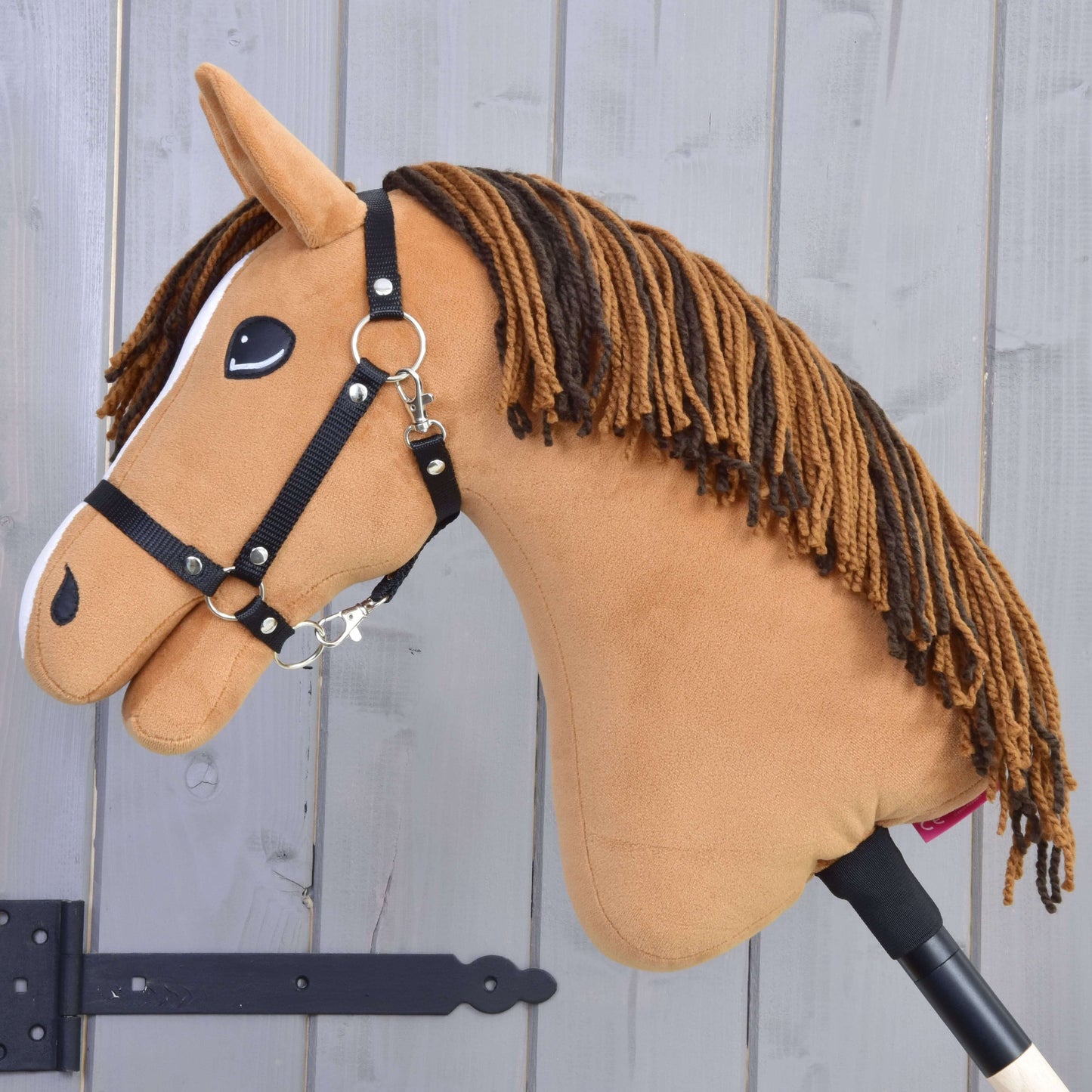 Hobby Horse Edward-LD s černou ohlávkou od Hobby Horse LarDen s plyšovým kaštanovým tělem, hnědou přízovou hřívou, černou ohlávkou a bílými detaily stojí před světle šedým dřevěným plotem.