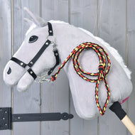 Hobby Horse LarDen "Hobby Horse - vodítko Flag", šedý plyšový Hobby Horse s tyčovým tělem, bílou hřívou, černou uzdečkou a pleteným červeným, žlutým a černým vodítkem, zobrazený na dřevěném pozadí.
