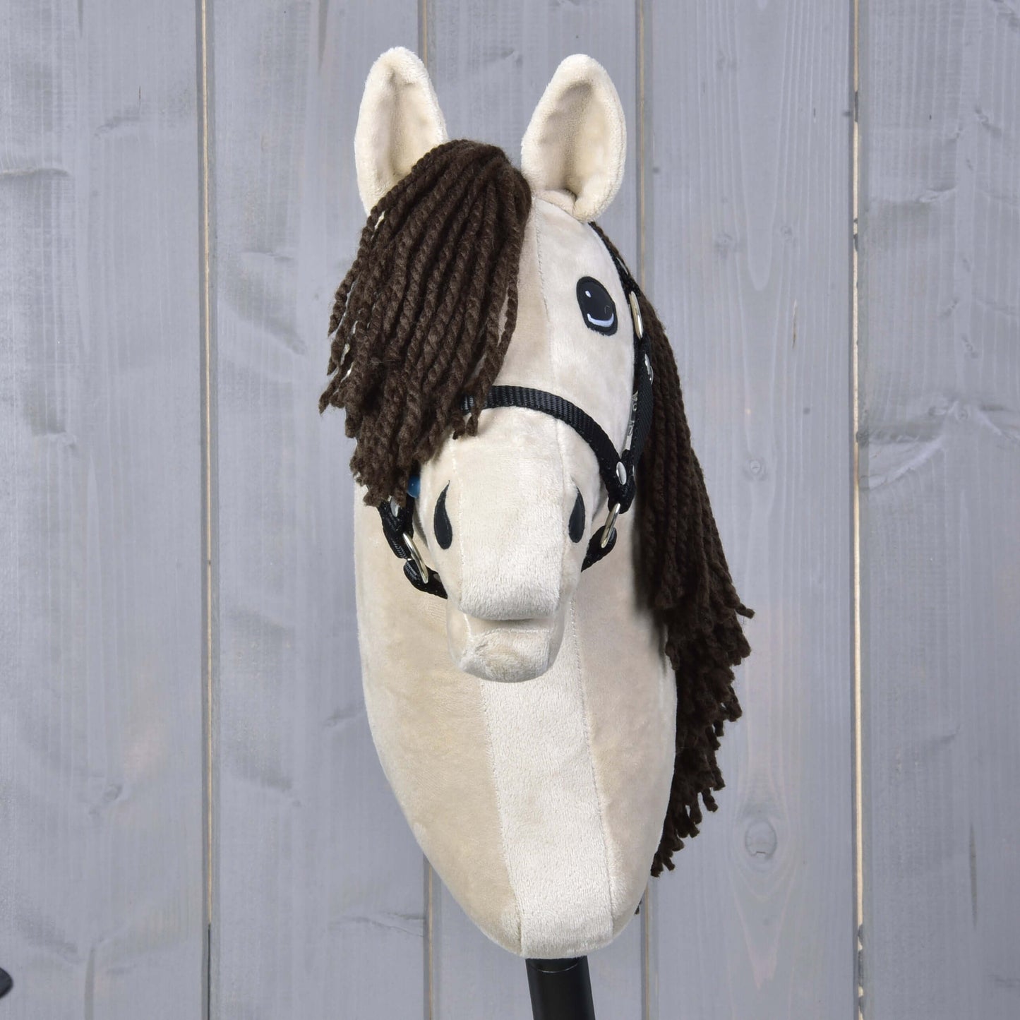Hobby Horse Frederik LD s černou ohlávkou od Hobby Horse LarDen, stojící vzpřímeně před světle šedým dřevěným plotem, s béžovým tělem a hnědou přízovou hřívou.
