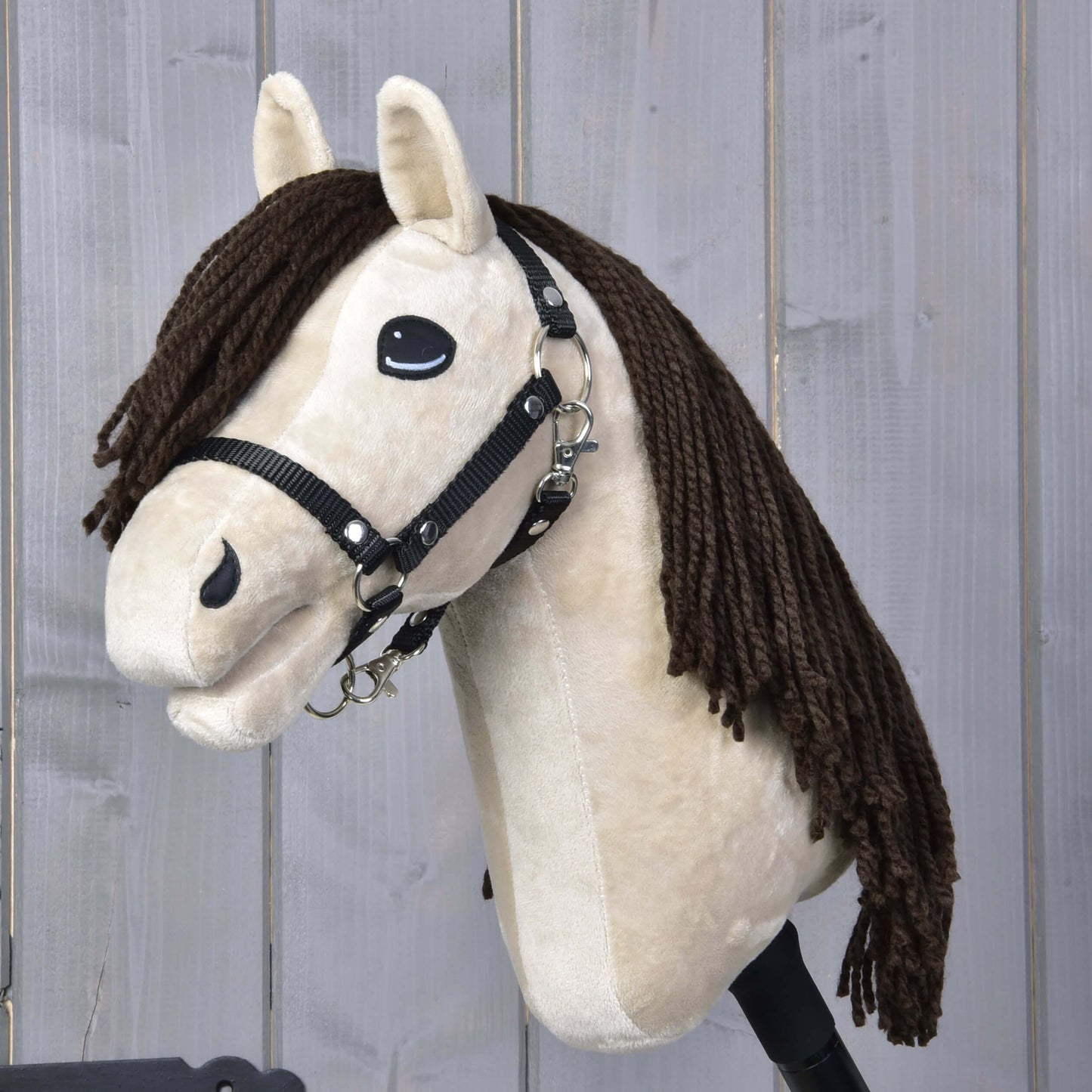 Hobby Horse Frederik LD s černou ohlávkou od Hobby Horse LarDen, s béžovým obličejem, černou ohlávkou a dlouhou hnědou přízovou hřívou, zobrazený na pozadí světle šedého dřeva.