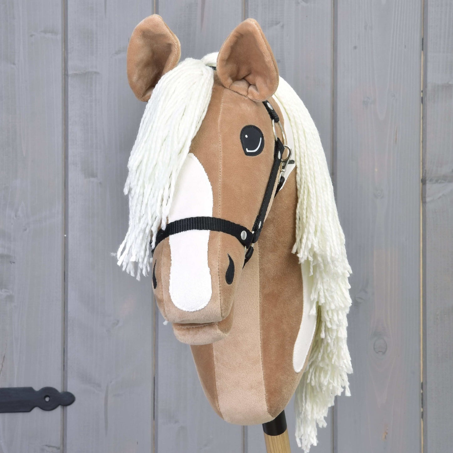 Hobby Horse Fury s černou ohlávkou od Hobby Horse LarDen má světle hnědý a bílý obličej, černou ohlávku a dlouhou bílou hřívu, připomíná American Paint Horse a je umístěný před šedým dřevěným pozadím. Ideální pro nápaditá dobrodružství.