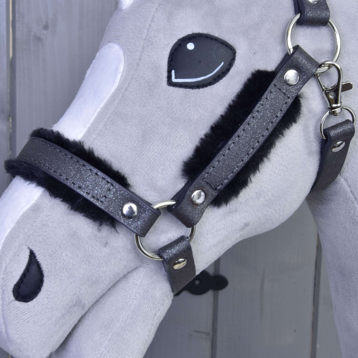 Detail šedobílé plyšové hlavy Hobby Horse s Ohlávkou s beránkem z koženky Graphite Full od Hobby Horse LarDen a vyšívanými detaily obličeje na dřevěném pozadí.