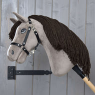 Hobby Horse Guccini s černou ohlávkou od Hobby Horse LarDen, s hnědou hřívou z příze a dřevěnou tyčí, na pozadí šedé stěny, ideální pro mladé fanoušky jezdeckého sportu.