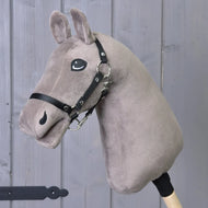 Build your horse od related_to_12441055625556, plyšový Hobby Horse v taupe barvě s černou uzdečkou a bílou přízovou hřívou na dřevěné tyči, zobrazený před pozadím z šedých dřevěných panelů.