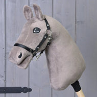 Build your horse od related_to_12441055625556, plyšový taupe Hobby Horse s hnědo-modrýma očima, černou uzdečkou a otěžemi, upevněný na dřevěné tyči, zobrazený na šedém dřevěném pozadí.