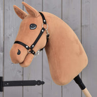 Hobby Horse Sestavte si svého koně od Hobby Horse LarDen s přizpůsobitelnou hnědou látkovou hlavou, černou uzdečkou a kreslenýma očima na dřevěné tyči, zobrazený před šedými dřevěnými dveřmi.