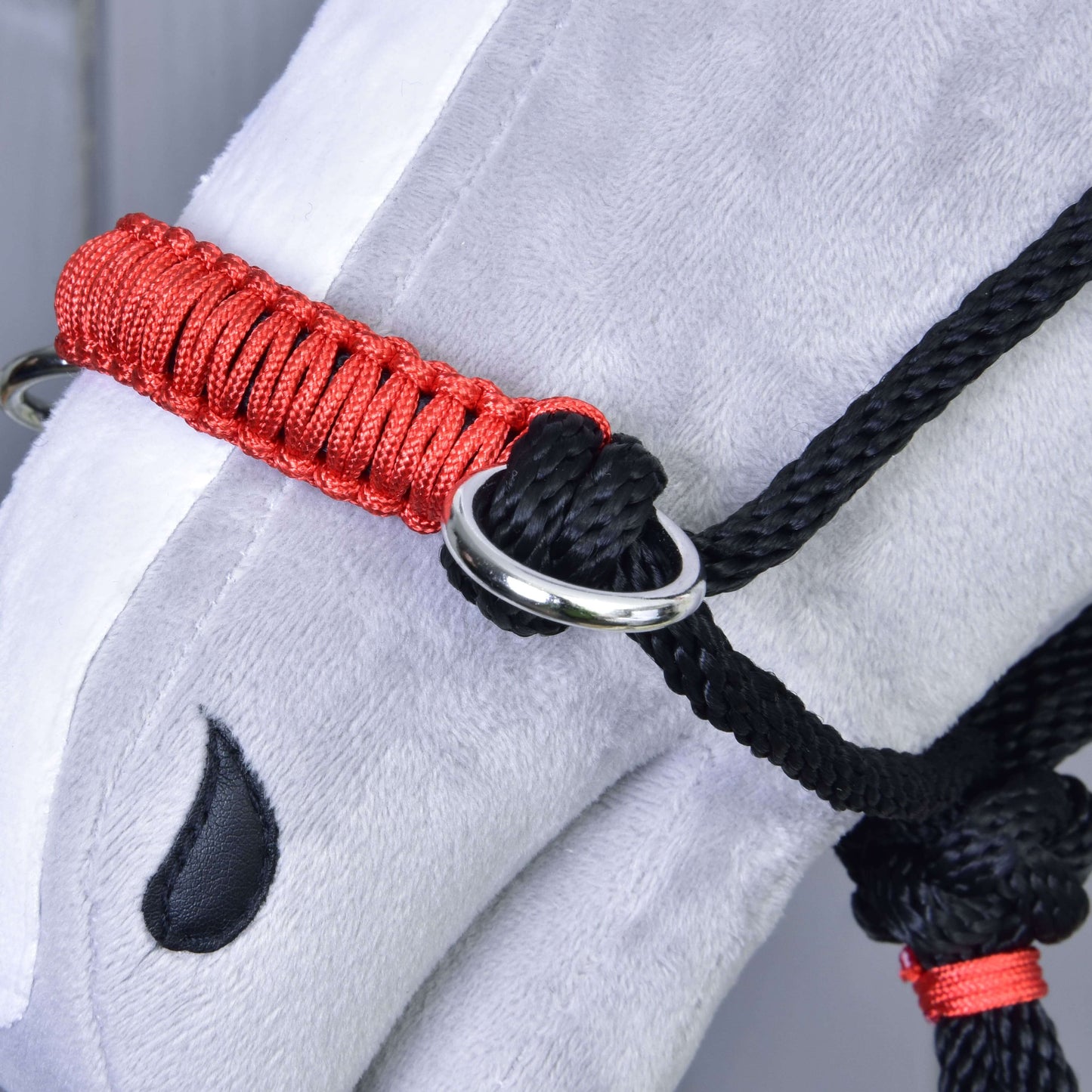 Detail hlavy šedého plyšového koně s Hobby Horse LarDen Parelka Jiskra v červené a černé barvě s kovovým kroužkem a černou vyšívanou slzou u oka. Ideální jako jedinečný doplněk pro Hobby Horse.