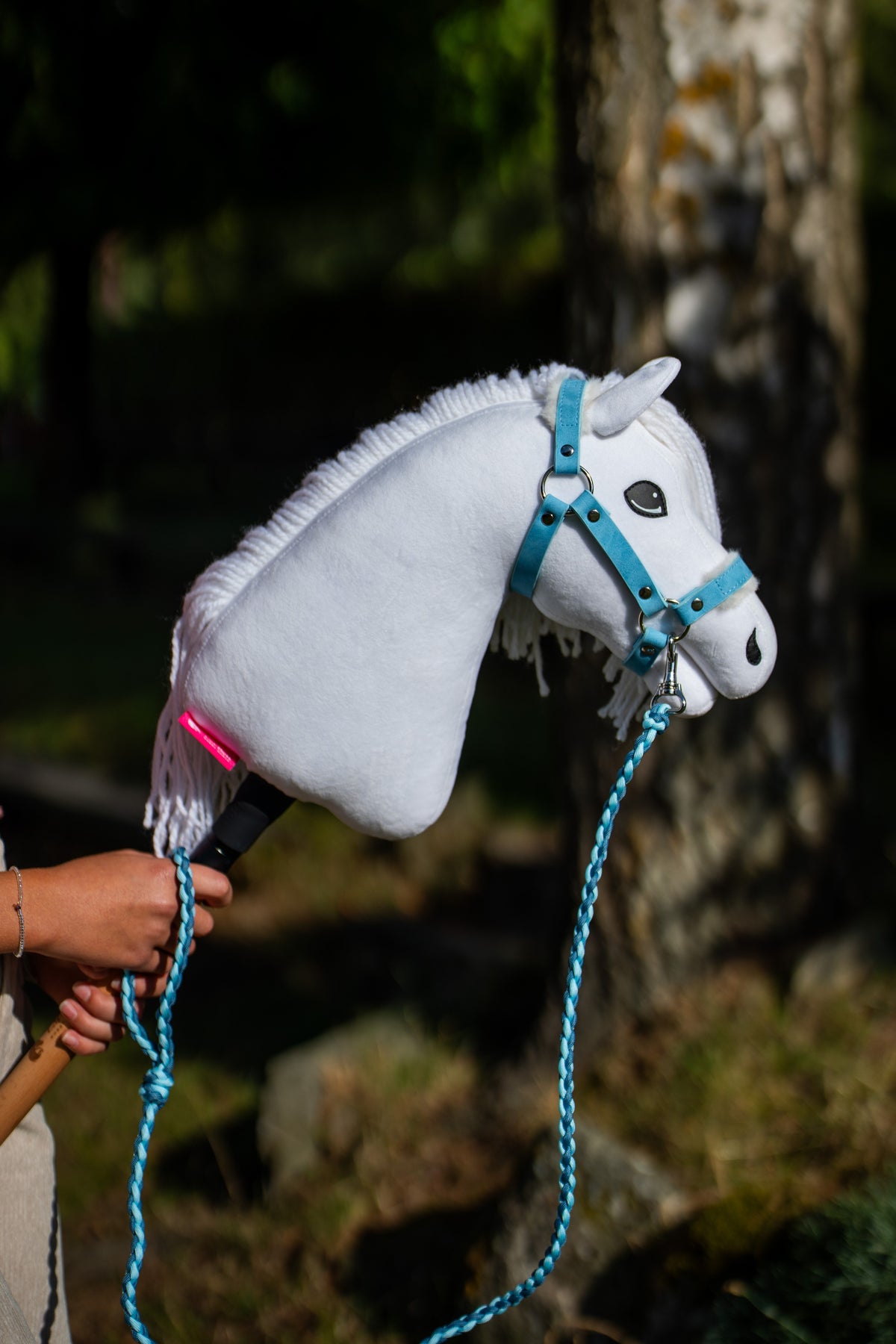 Hlava Hobby Horse Lady s černou ohlávkou od Hobby Horse LarDen držená ve skvrnitém stínu, bílý plyš, tmavé oko, bílá přízová hříva, s ohlávkou Pastell Blue s kožešinou z koženky a pleteným vodítkem Double Blue