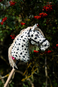 Hobby Horse Lord Valentine s černou ohlávkou od LarDen stojí před jeřábem s trsy červených bobulí, s bílou plyšovou hlavou s černými leopardími skvrnami, krémovou přízovou hřívou a černou ohlávkou se stříbrným kováním