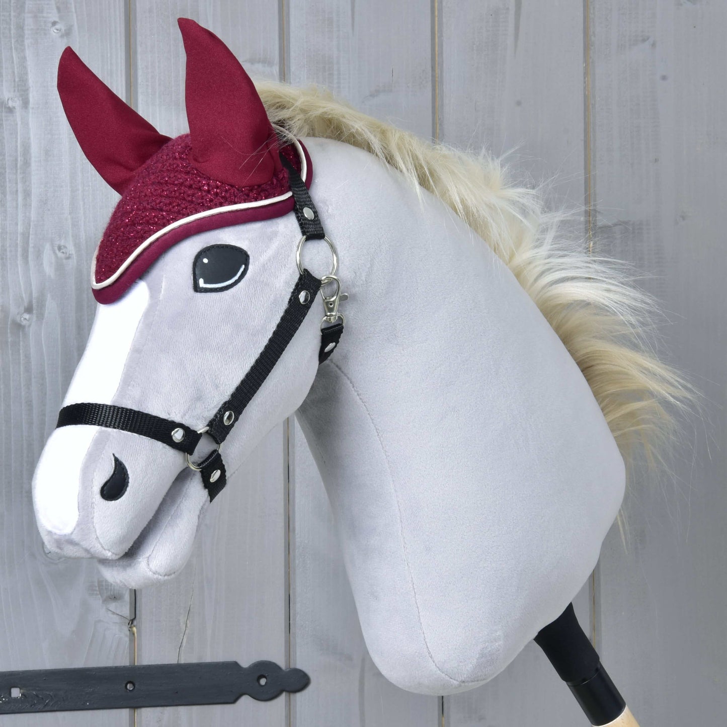 Čabraka Lux Maroon od Hobby Horse LarDen na plyšovém koni na tyči s bílým obličejem, černou uzdečkou, huňatou blond hřívou, kaštanovými látkovými ušima a ladící čabrakou na šedém dřevěném pozadí.