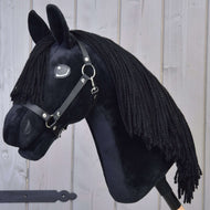 Hobby Horse Mahal s černou ohlávkou od Hobby Horse LarDen je plyšový Hobby Horse ve stylu fríského koně s černou hřívou, černou ohlávkou a bílým detailem u oka, upevněný na dřevěné tyči a zobrazený před světle šedou dřevěnou stěnou.