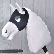 Plyšový Hobby Horse se světle šedou srstí, bílou hřívou a černou uzdečkou má na sobě masku Maska bez uší Flamingo od Hobby Horse LarDen a je nasazený na dřevěné tyči před pozadím z šedých dřevěných panelů.