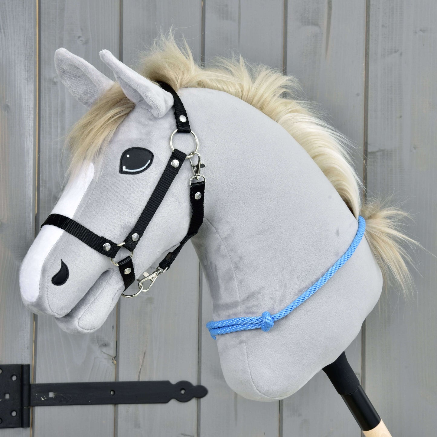 Nákrčník Sky od Hobby Horse LarDen je šedý plyšový Hobby Horse s bílou hřívou, černou uzdečkou a modrým lanem, navržený pro ježdění s uzdečkou i bez ní. Stojí před dřevěným pozadím a má přátelský výraz.