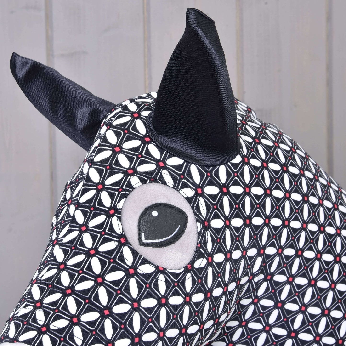 Detail Hobby Horse ochranného obleku DeLuxe (Lycra) od Hobby Horse LarDen z pratelné černobílé geometrické lycry s velkýma černýma ušima a prošívaným okem na světlém dřevěném pozadí.