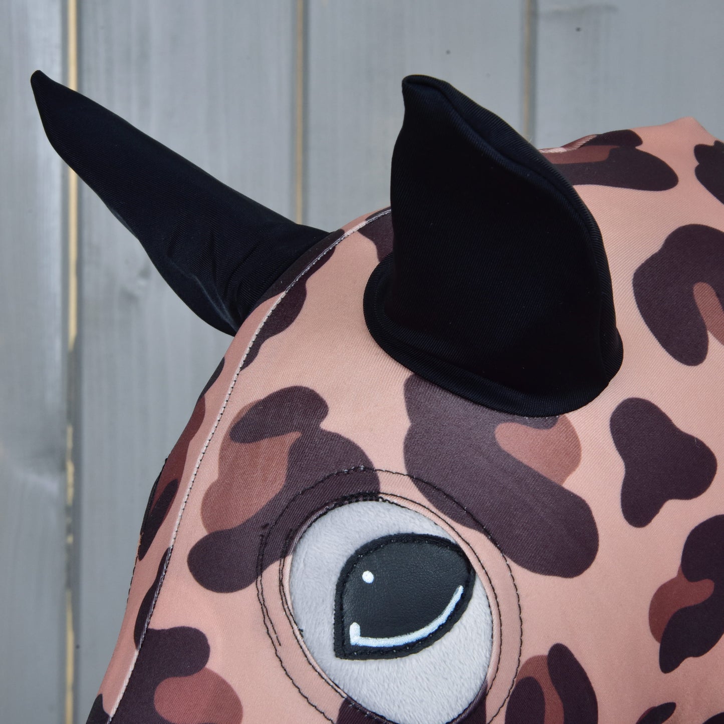 Detail Hobby Horse ochranného obleku Glamour (Lycra) od Hobby Horse LarDen s leopardí látkou, velkým vyšívaným okem a dvěma černými špičatými ušima, připomínající hravého Hobby Horse na světlém dřevěném pozadí.