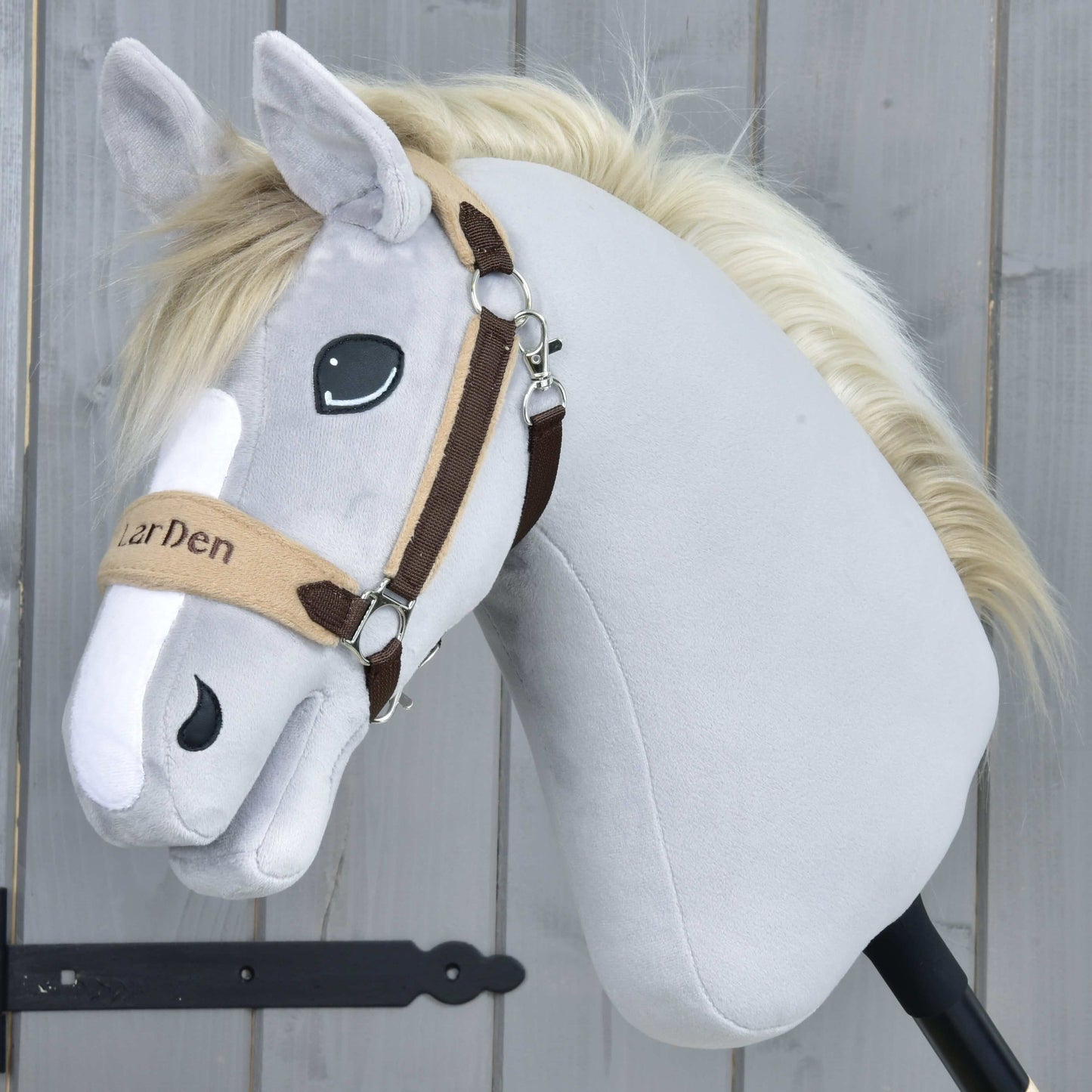Hobby Horse LarDen Ohlávka s beránkem LarDen Brown se světle šedým plyšem, krémovou hřívou, béžovohnědou ohlávkou s měkkým fleecovým nánosníkem, vyšívanýma očima a přátelským výrazem na dřevěném pozadí.