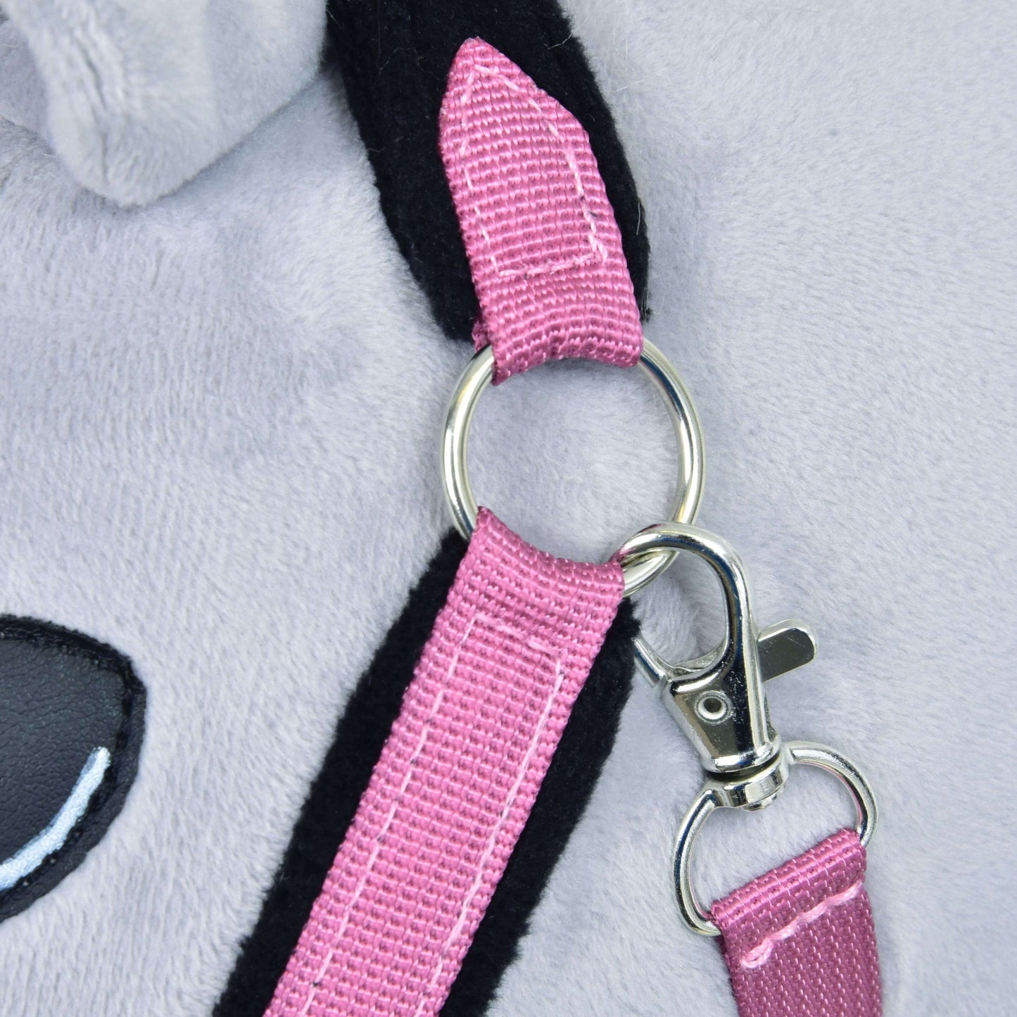 Ohlávka s beránkem LarDen Pink od Hobby Horse LarDen, detail světle šedého plyšového povrchu, lesklého kovového kroužku na popruhu růžové kožešinové ohlávky, stříbrné přezky a části černorůžového ucha s černým okem.