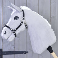 Šedý plyšový Hobby Horse od Hobby Horse LarDen s bílou hřívou a ohlávkou Ohlávka - černá koženka, nasazený na dřevěné tyči na pozadí dřevěných panelů.