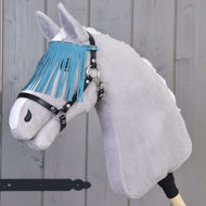 Šedý Hobby Horse LarDen s černou ohlávkou s tyrkysovými třásněmi stojí před dřevěnou stěnou.