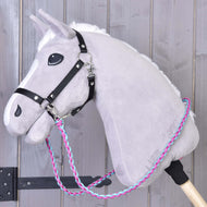 Hobby Horse LarDen „Otěže knitted pinkie blue“, šedý plyšový Hobby Horse s černou uzdečkou a ručně pletenými růžovými, modrými a bílými otěžemi na dřevěné tyči, zobrazený na světlém dřevěném pozadí.