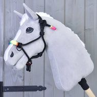 Parelka Duha od Hobby Horse LarDen na šedém Hobby Horse s bílou hřívou, duhově barevnými korálky a černou provazovou ohlávkou na dřevěné tyči, před světle šedou dřevěnou stěnou.