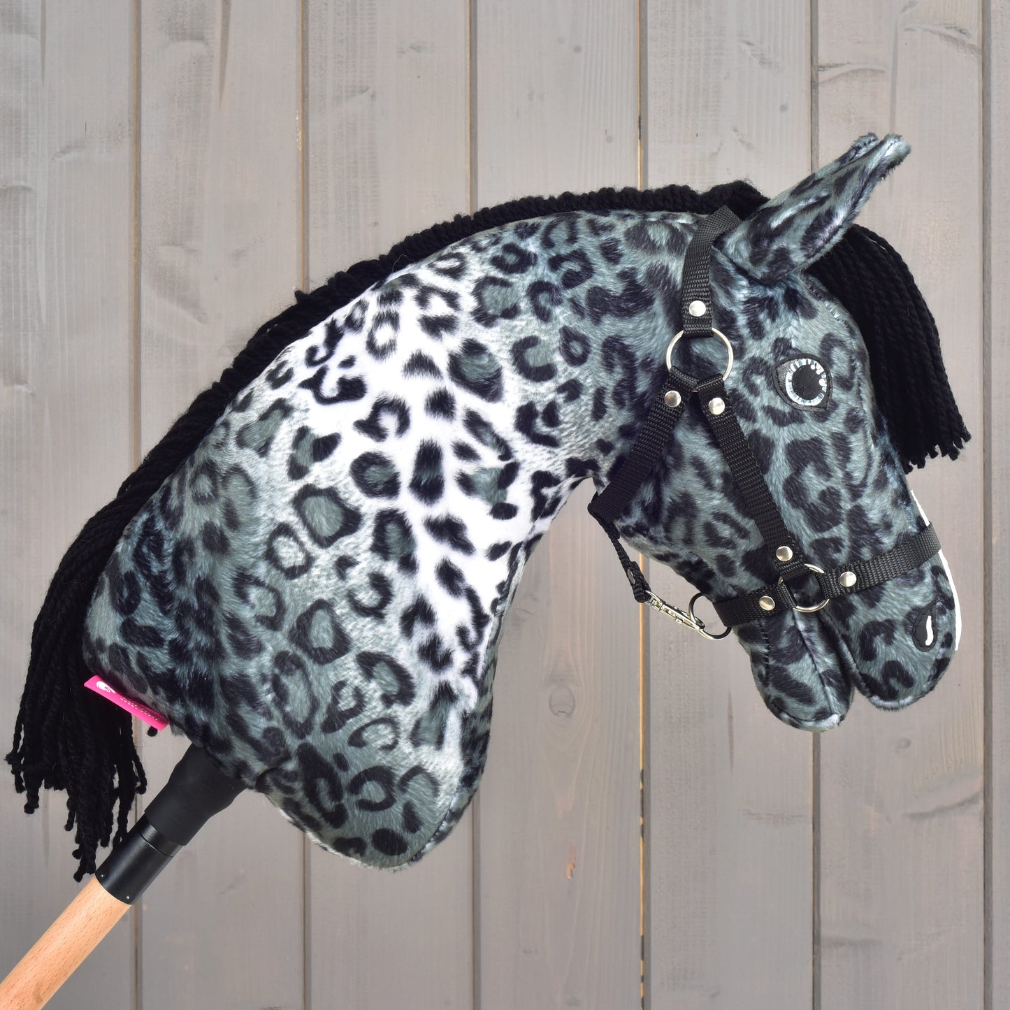 Hobby Horse Picasso s černou ohlávkou od Hobby Horse LarDen s měkkým černobílým leopardím vzorem inspirovaným skvrnitou srstí appaloosy, doplněný černou přízovou hřívou a černou ohlávkou, zobrazený na dřevěném pozadí.