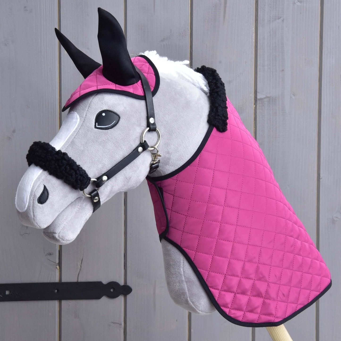 Hobby Horse LarDen Set Pink Beauty (čabraka + deka + ohlávka s beránkem) s plyšovým hračkovým Hobby Horse s prošívanou růžovou dekou, ladící čabrakou a ohlávkou s kožešinovým lemem — základní doplňky — před dřevěnými prkny.