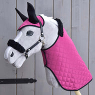 Hobby Horse LarDen Set Pink Beauty (čabraka + deka + ohlávka s beránkem) s plyšovým hračkovým Hobby Horse s prošívanou růžovou dekou, ladící čabrakou a ohlávkou s kožešinovým lemem — základní doplňky — před dřevěnými prkny.